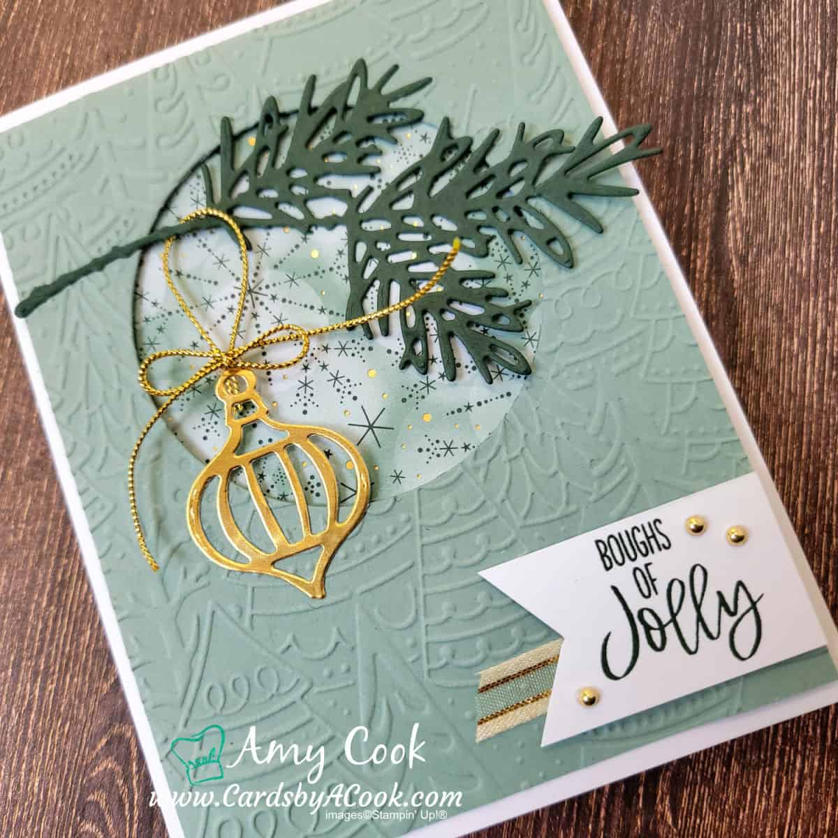 Christmas card featuring a Christmas tree bough hung with a gold ornament and a gold bow. Greeting reads Boughs of Jolly